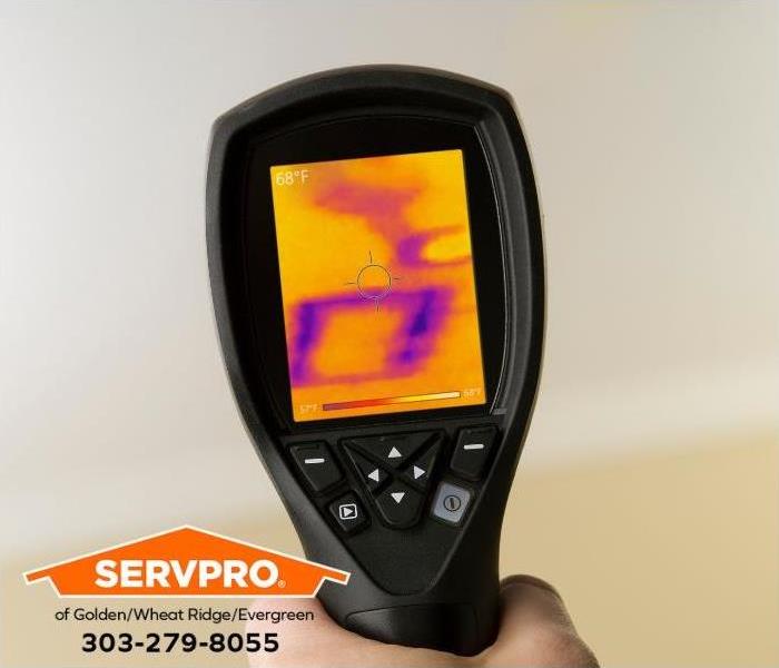 A person uses an infrared camera to locate hidden water damage in a room.